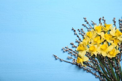 Photo of Bouquet of beautiful yellow daffodils and willow flowers on light blue wooden table, top view. Space for text