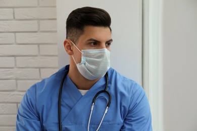 Sad doctor near window indoors. Stress of health care workers during coronavirus pandemic