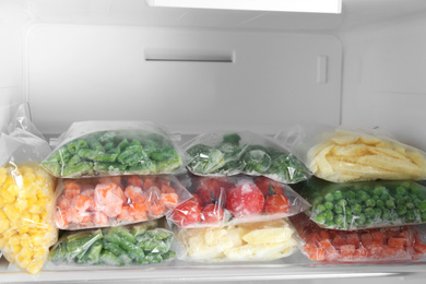 Plastic bags with different frozen vegetables in refrigerator