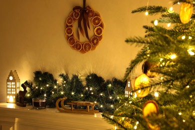 Photo of Fireplace with Christmas accessories and decorative wreath near fir tree indoors