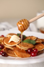 Photo of Pouring honey onto cereal pancakes with cranberries at white wooden table, closeup