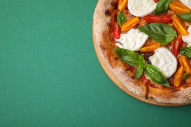 Delicious pizza with burrata cheese, tomatoes and basil on green background, top view. Space for text