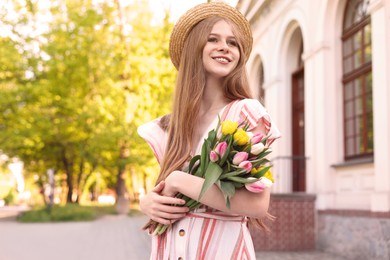 Photo of Beautiful teenage girl with bouquet of tulips on city street, space for text