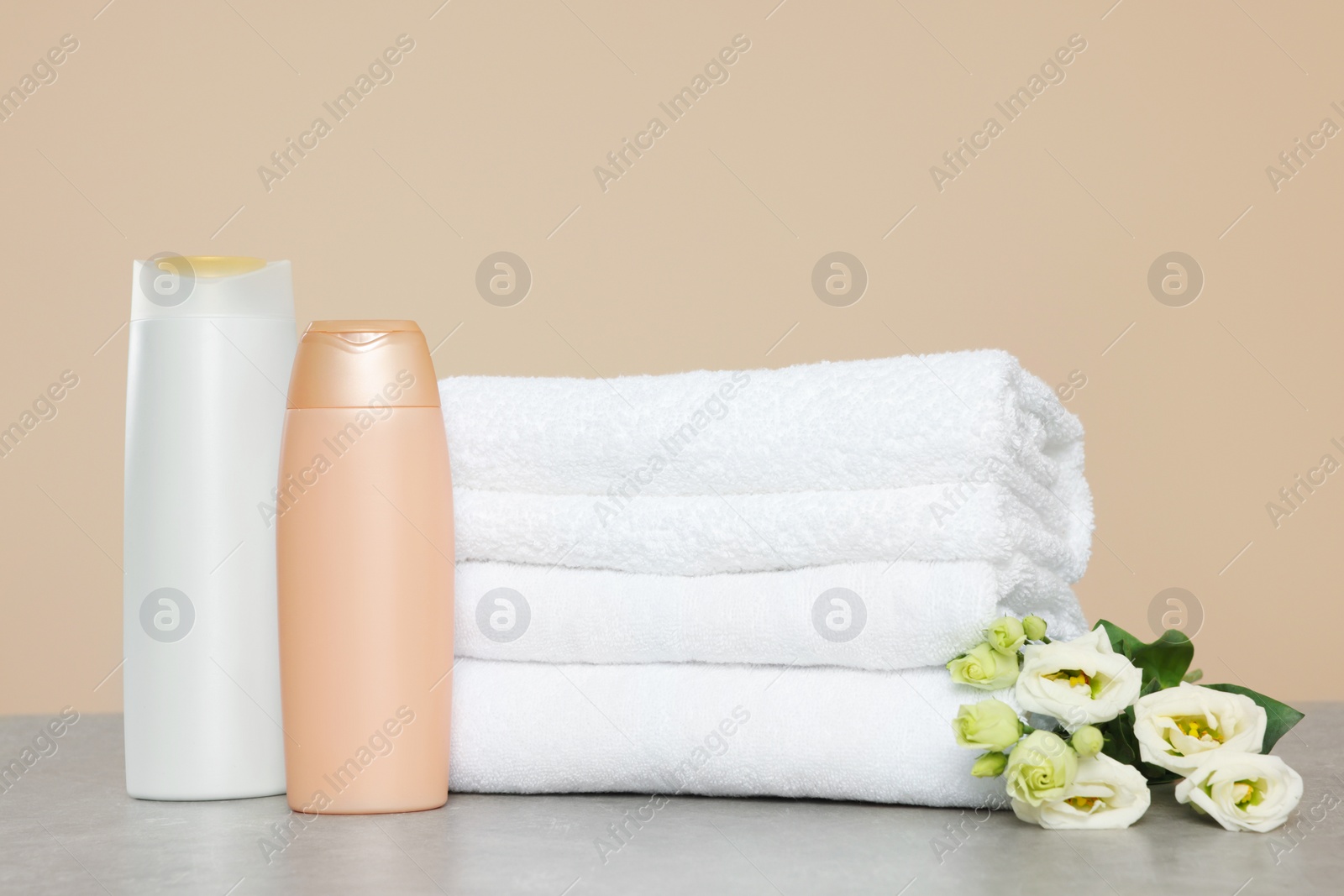 Photo of Soft folded towels, bottles of cosmetic products and eustoma flowers on grey table