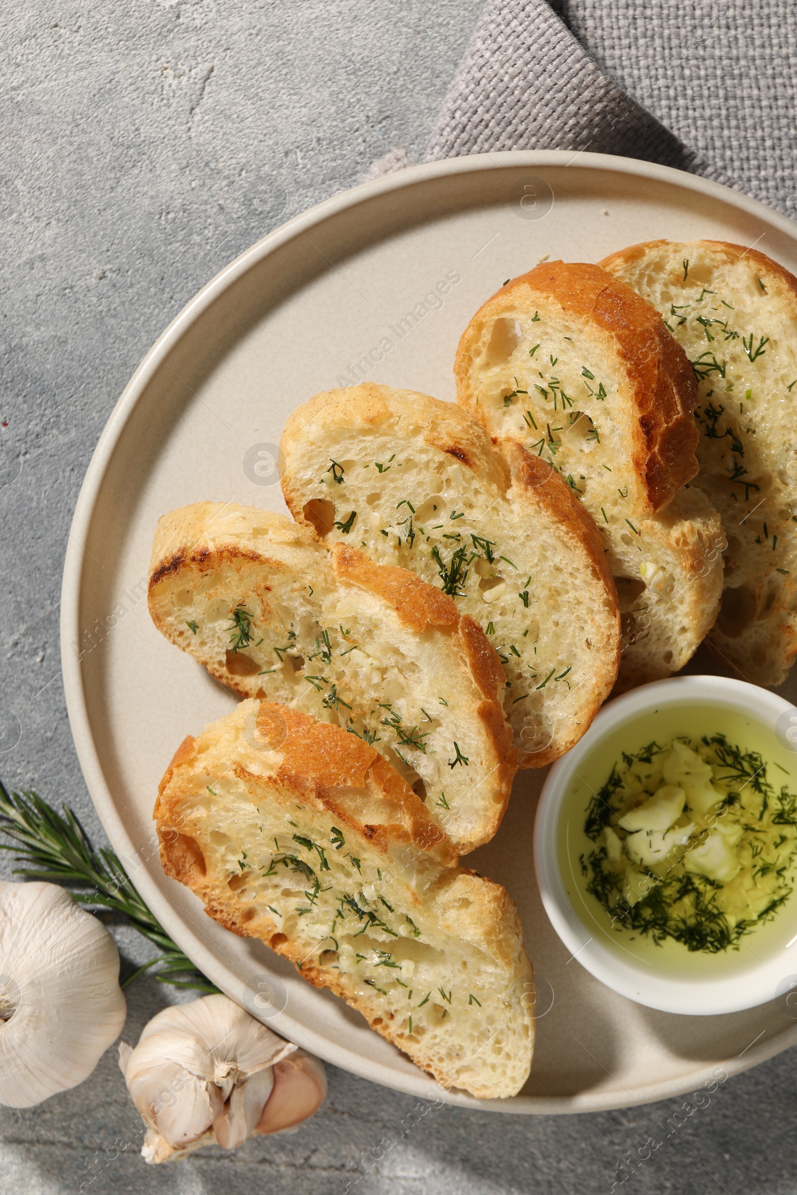 Photo of Tasty baguette with garlic and dill served on grey textured table, top view