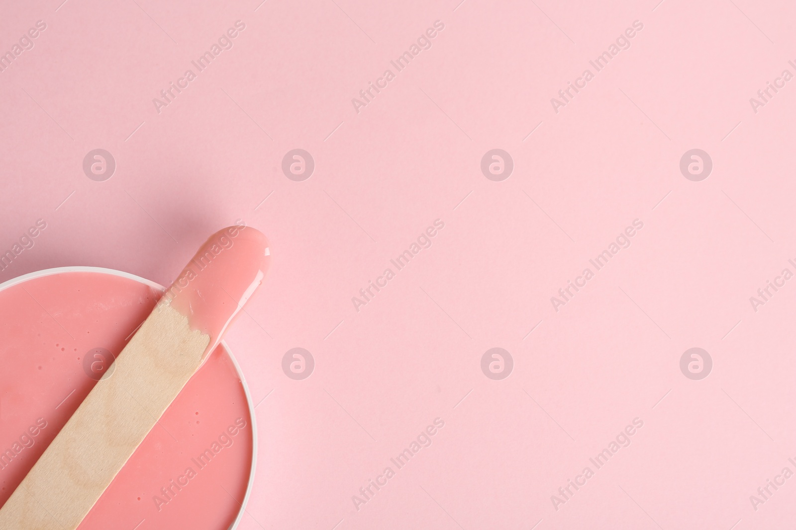 Photo of Wooden spatula and hot depilatory wax on light pink background, top view. Space for text