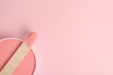 Wooden spatula and hot depilatory wax on light pink background, top view. Space for text