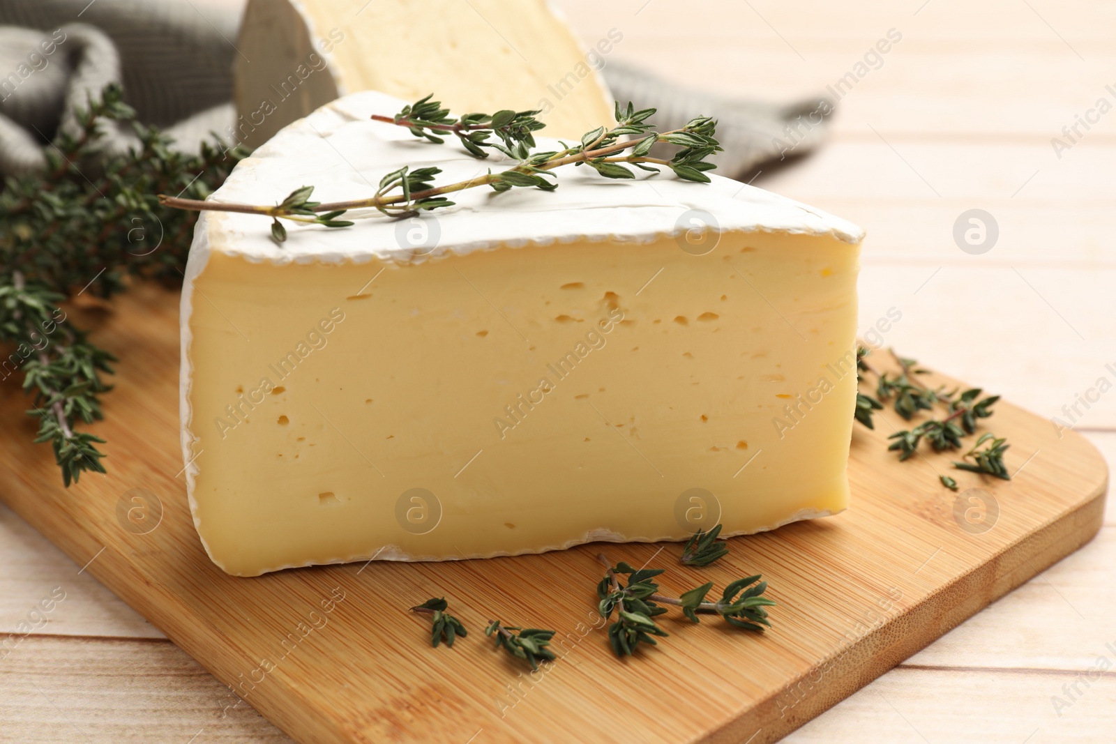 Photo of Board with pieces of tasty camembert cheese and thyme on light wooden table, closeup