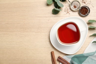 Freshly brewed rooibos tea, dry leaves and spices on wooden table, flat lay. Space for text