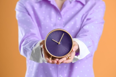 Young woman holding alarm clock on color background. Time concept