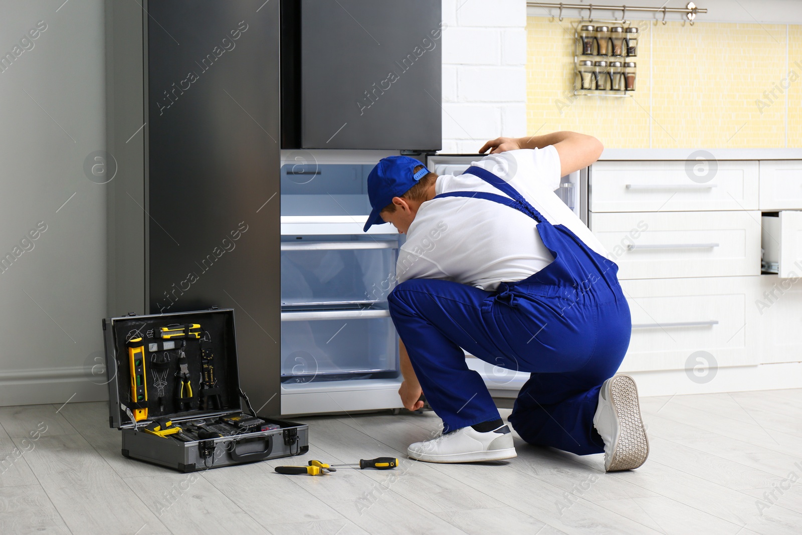 Photo of Male technician repairing broken refrigerator in kitchen