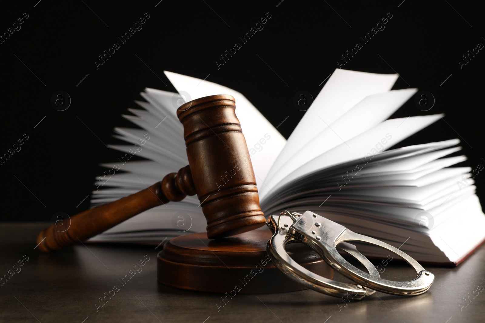 Photo of Judge's gavel, handcuffs and book on grey table against black background. Criminal law concept