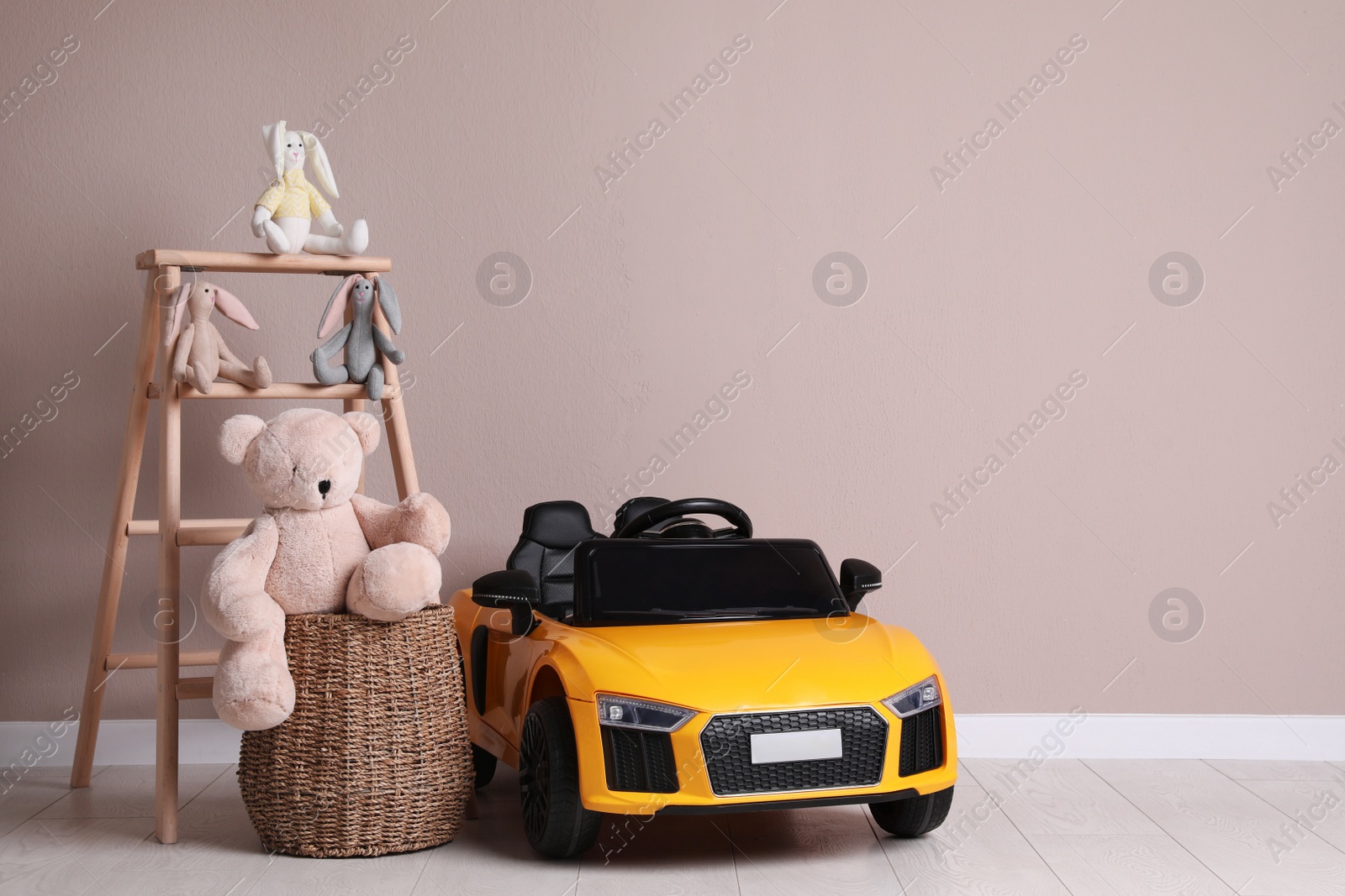 Photo of Child's electric car with other toys near beige wall indoors. Space for text