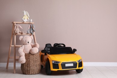 Child's electric car with other toys near beige wall indoors. Space for text