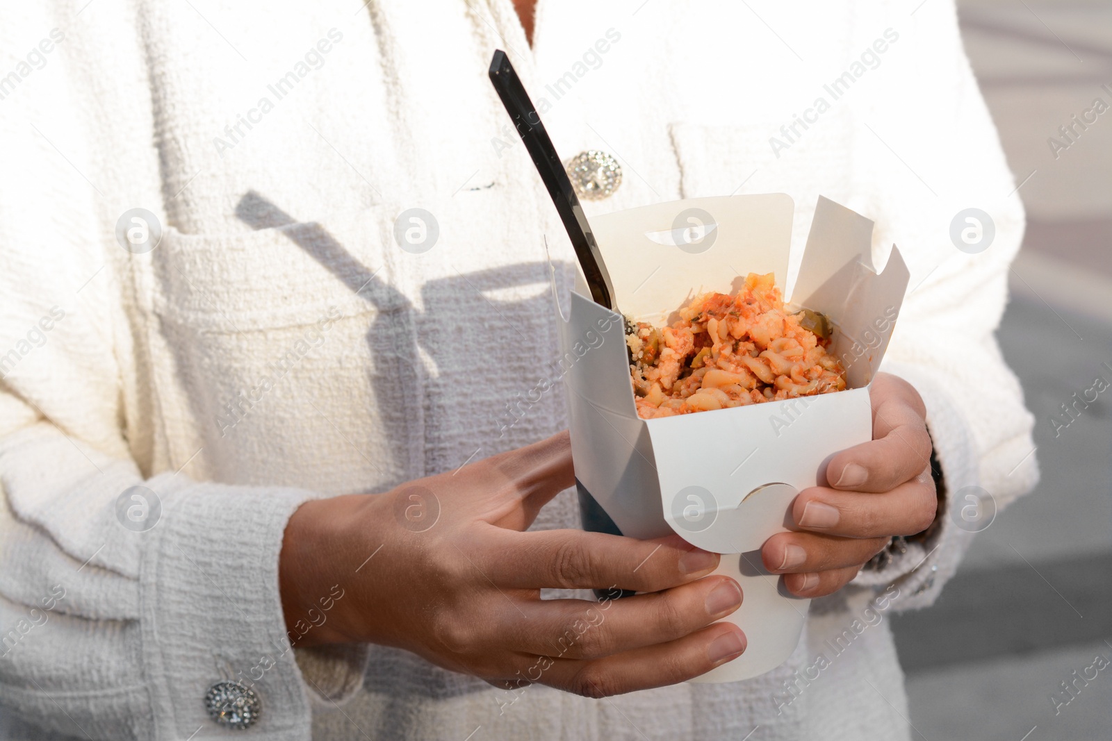 Photo of Woman holding paper box of takeaway noodles with fork outdoors, closeup. Street food