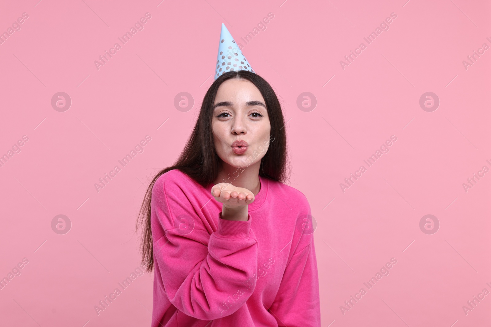 Photo of Woman in party hat blowing kiss on pink background