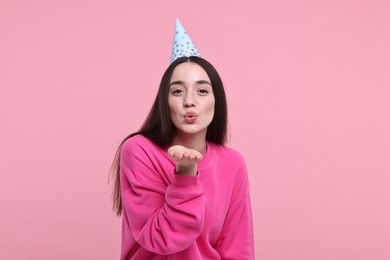 Photo of Woman in party hat blowing kiss on pink background