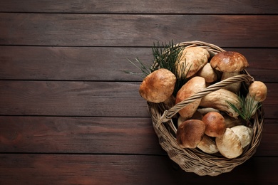 Photo of Fresh wild mushrooms in wicker basket on wooden table, top view. Space for text