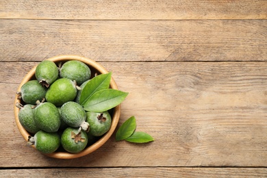 Photo of Top view of fresh green feijoa fruits in bowl on wooden table, space for text