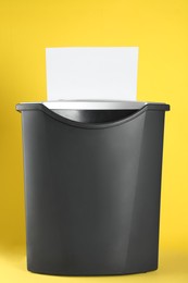 Shredder with sheet of white paper on yellow background