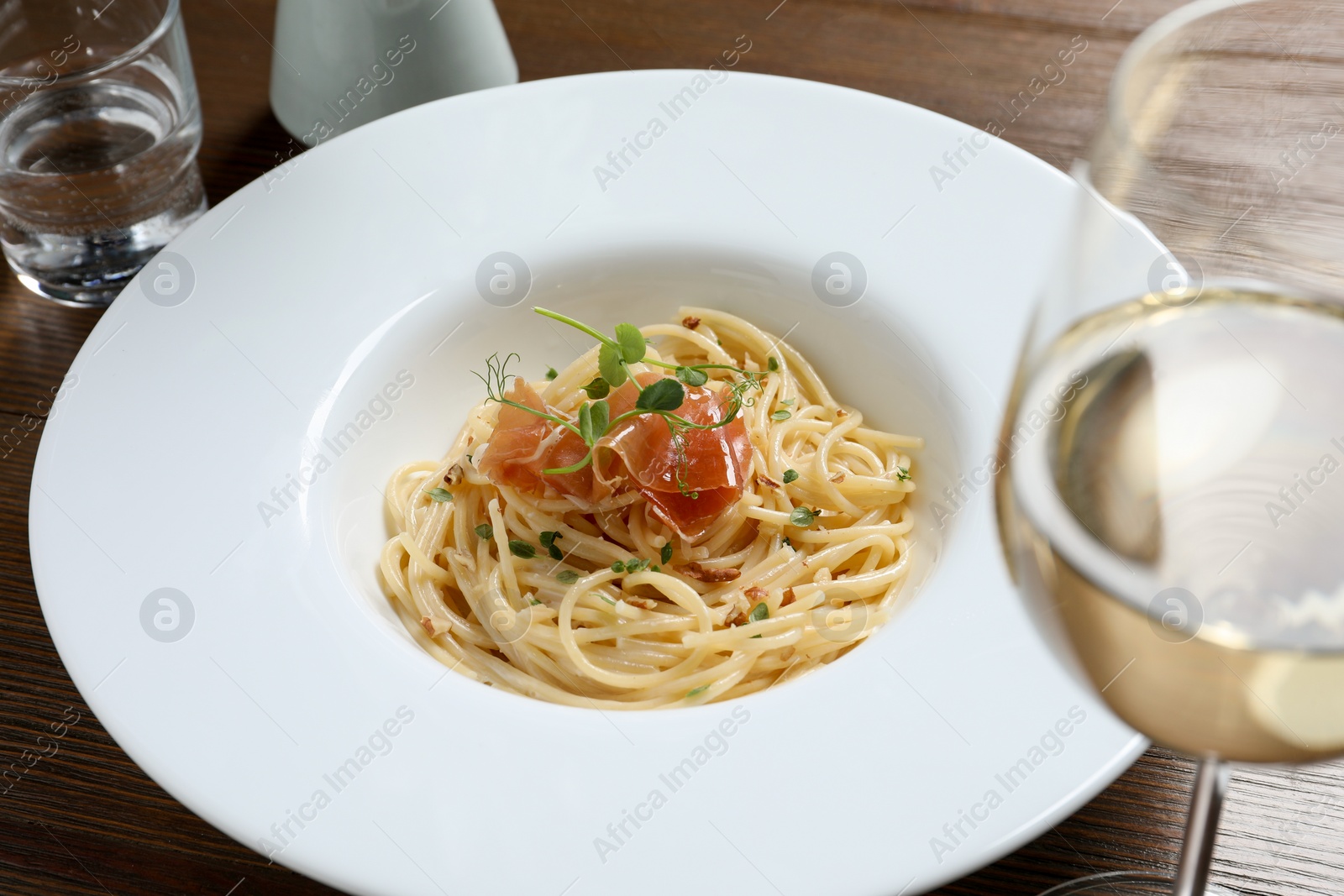 Photo of Tasty spaghetti with prosciutto and microgreens served on wooden table, closeup. Exquisite presentation of pasta dish