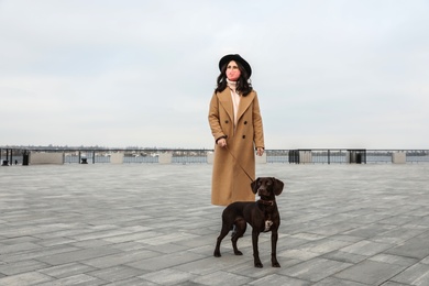 Woman in protective mask with German Shorthaired Pointer outdoors. Walking dog during COVID-19 pandemic