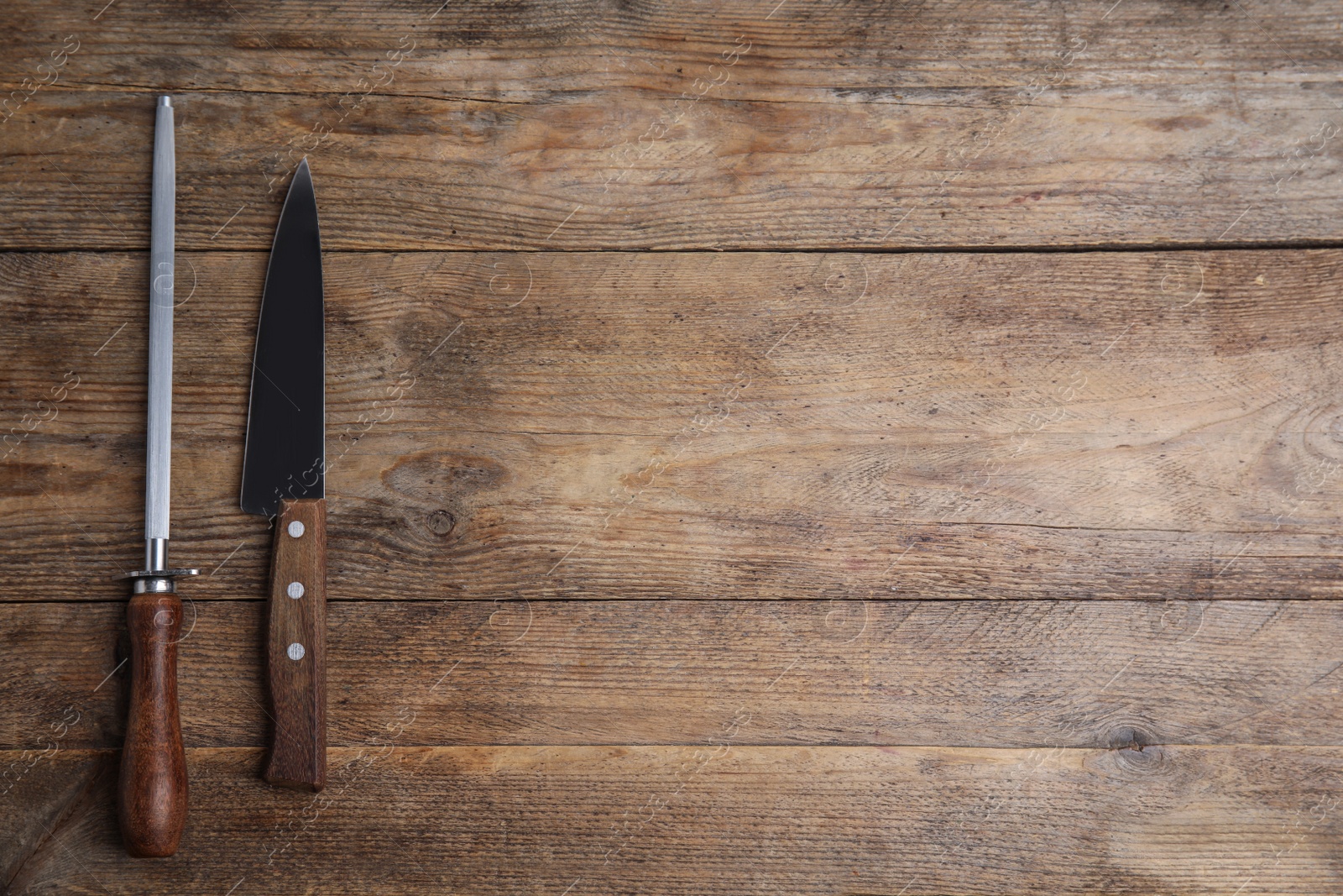 Photo of Sharpening steel and knife on wooden table, flat lay. Space for text