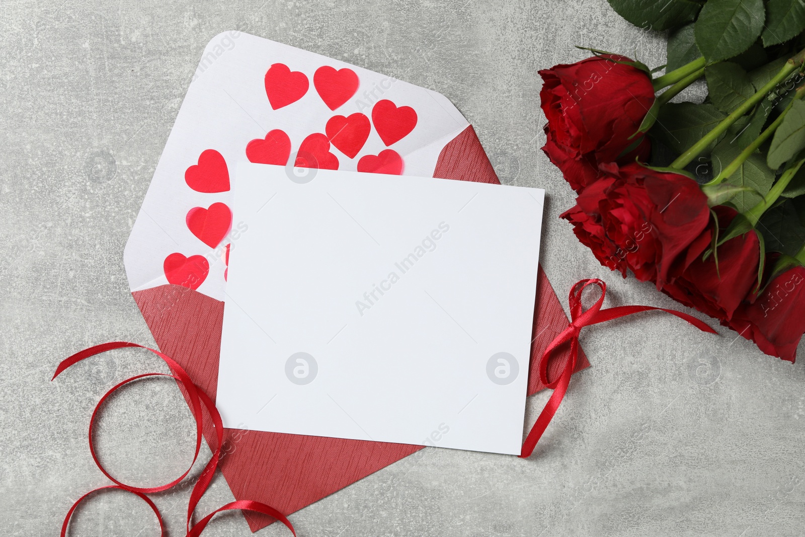 Photo of Flat lay composition with blank greeting card and roses on light grey stone table. Valentine's day celebration