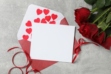 Photo of Flat lay composition with blank greeting card and roses on light grey stone table. Valentine's day celebration