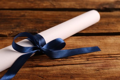 Rolled student's diploma with blue ribbon on wooden table, closeup