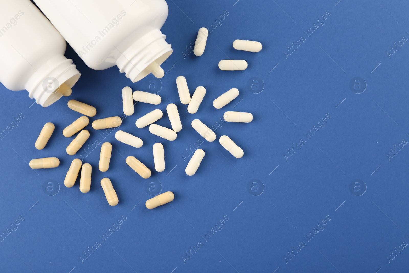 Photo of Bottles and different vitamin capsules on blue background, flat lay. Space for text