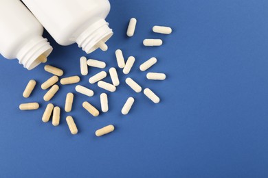 Bottles and different vitamin capsules on blue background, flat lay. Space for text