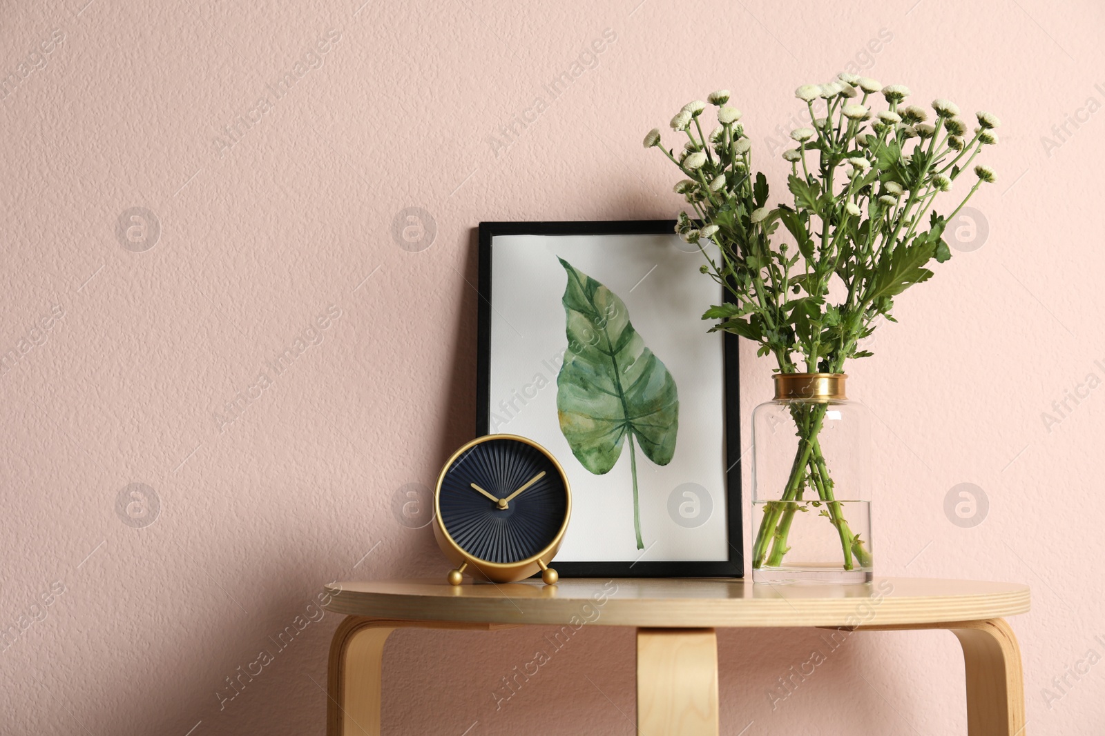 Photo of Composition with chrysanthemum flowers in glass vase on wooden table near pink wall. Space for text