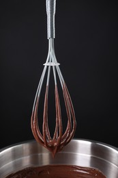 Chocolate cream flowing from whisk into bowl on black background