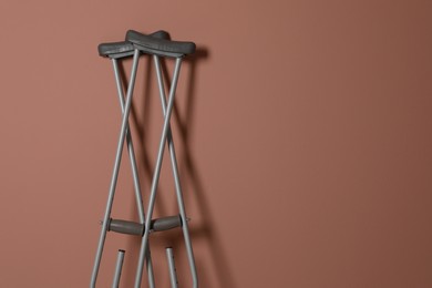 Photo of Pair of axillary crutches on pale pink background. Space for text