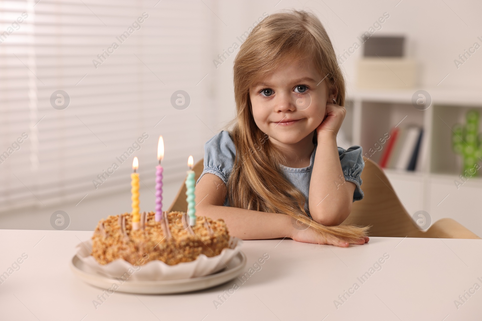 Photo of Cute girl with birthday cake at table indoors