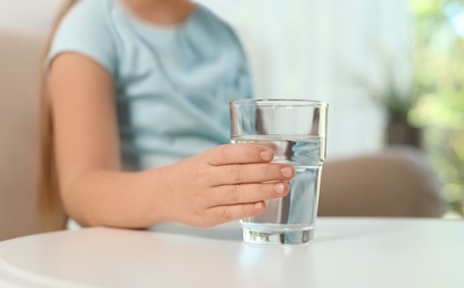 Photo of Cute little girl holding glass of fresh water indoors, closeup