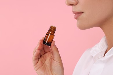 Photo of Woman with bottle of essential oil on pink background, closeup