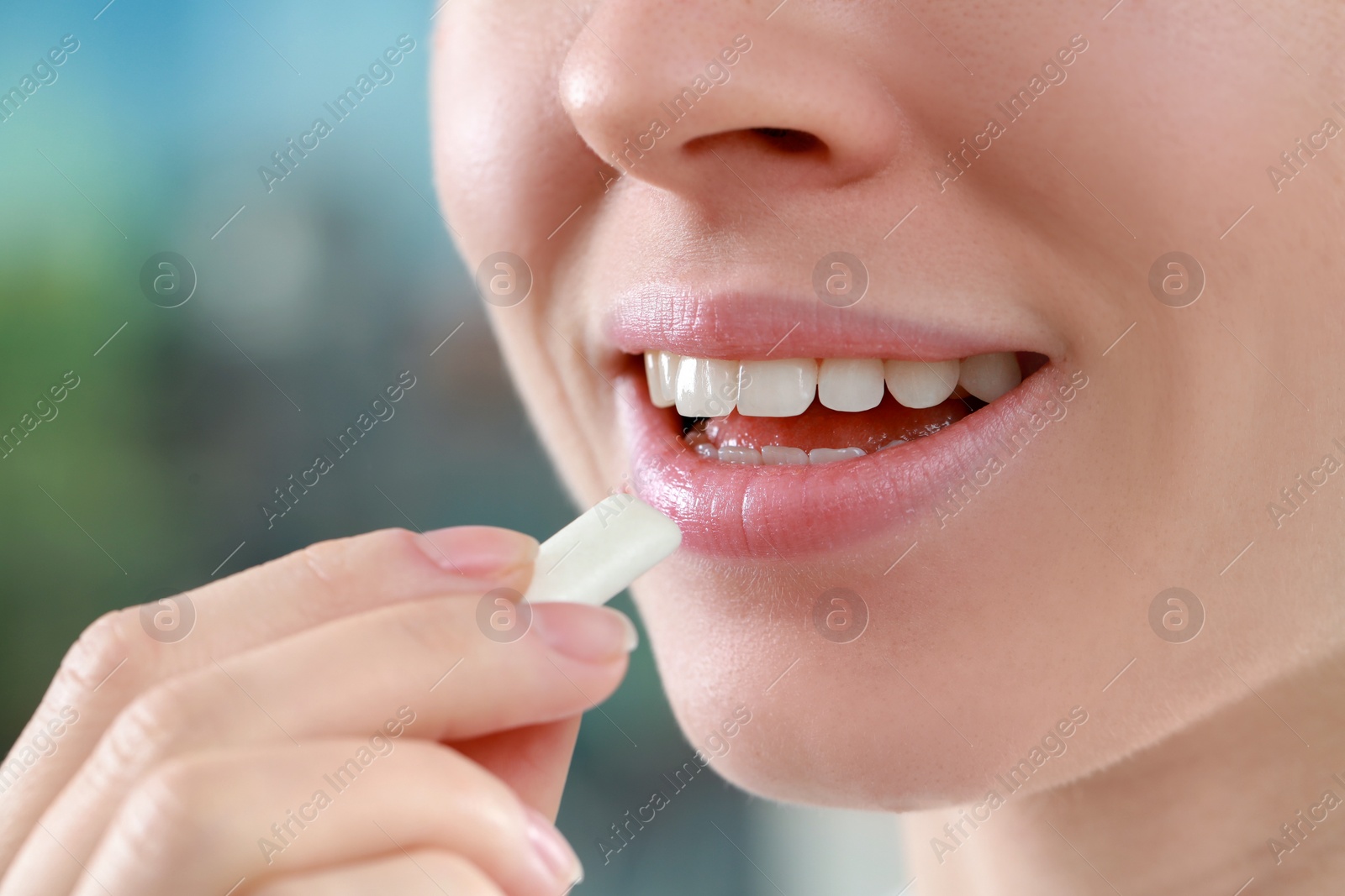 Photo of Woman putting chewing gum piece into mouth on blurred background, closeup