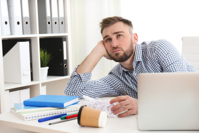 Lazy young man wasting time at messy table in office