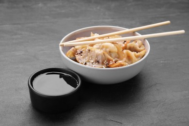 Photo of Delicious gyoza (asian dumplings), soy sauce and chopsticks on dark grey table