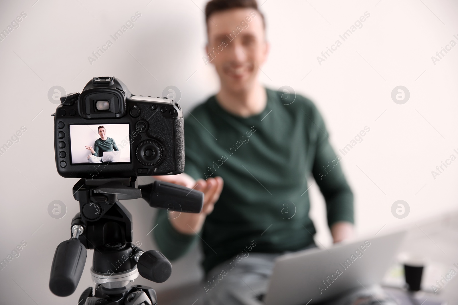 Photo of Male blogger with laptop on camera screen near light wall, closeup