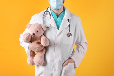 Pediatrician with teddy bear and stethoscope on yellow background, closeup