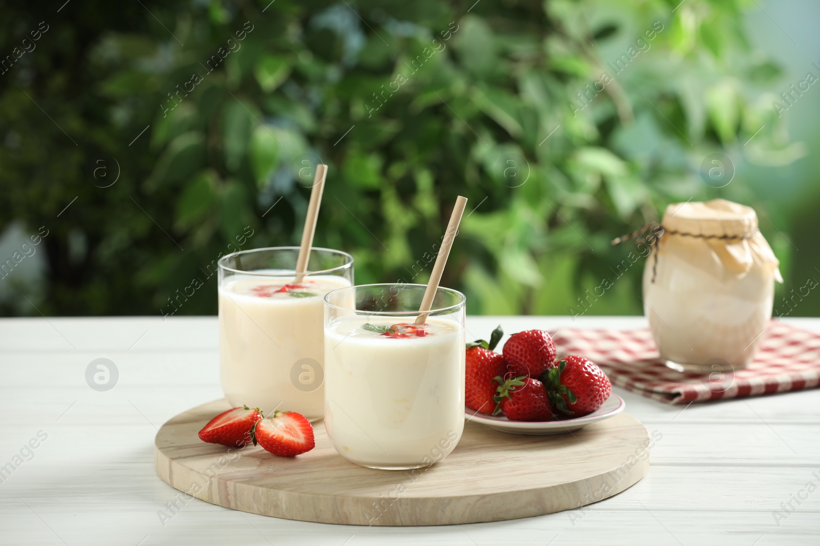 Photo of Tasty yogurt in glasses and strawberries on white wooden table outdoors