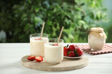 Photo of Tasty yogurt in glasses and strawberries on white wooden table outdoors
