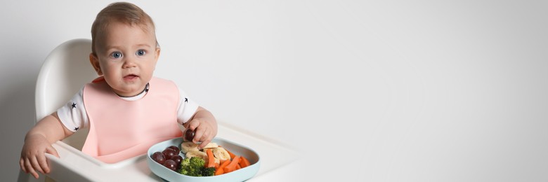 Image of Cute little baby wearing bib while eating on white background, space for text. Banner design