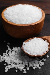Photo of Spoon and bowl of natural sea salt on wooden table, closeup