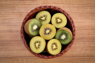 Photo of Bowl of many cut fresh kiwis on wooden table, top view