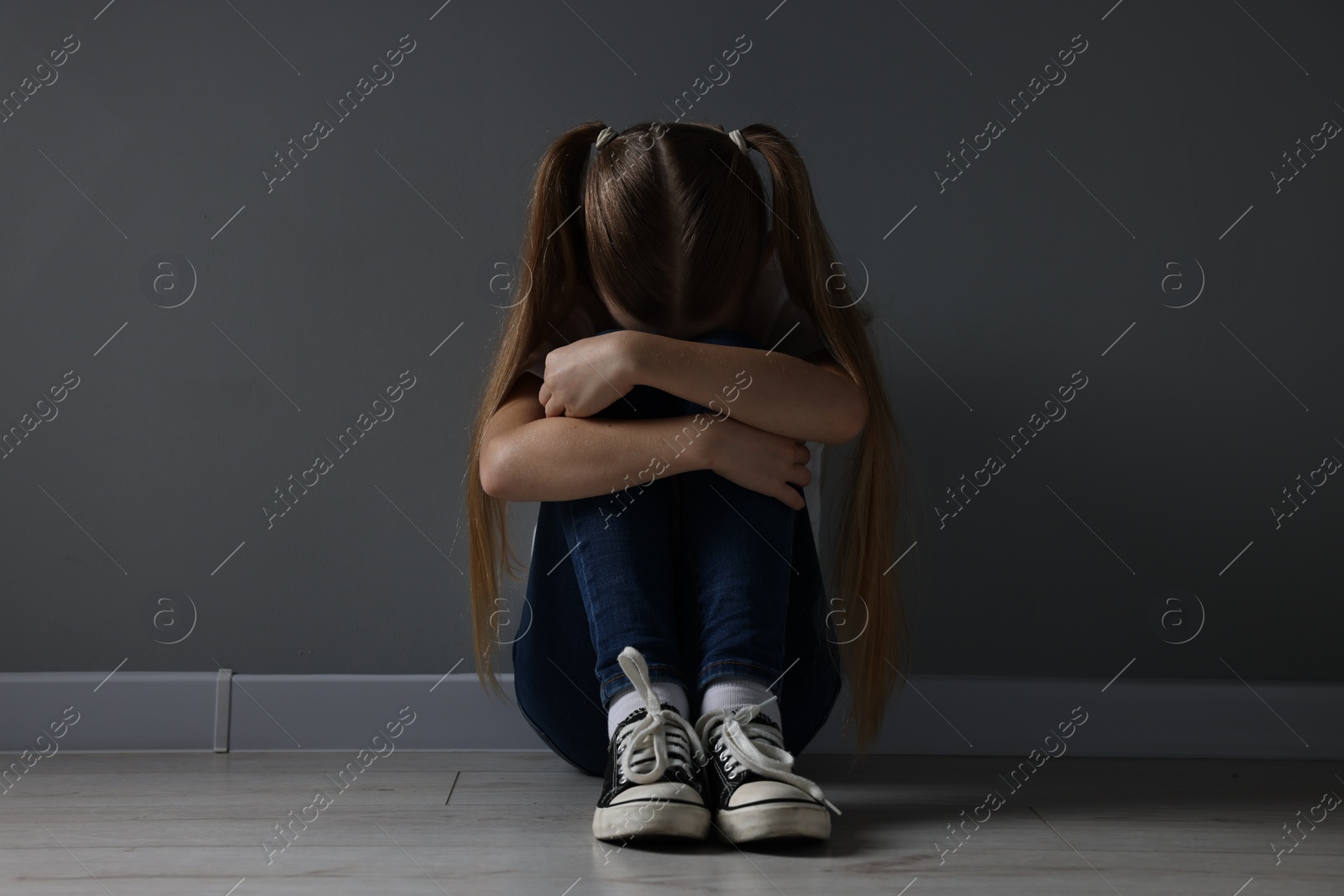 Photo of Sad girl sitting on floor near dark grey wall indoors