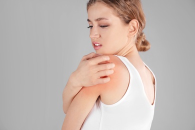 Woman scratching shoulder on grey background. Allergy symptoms